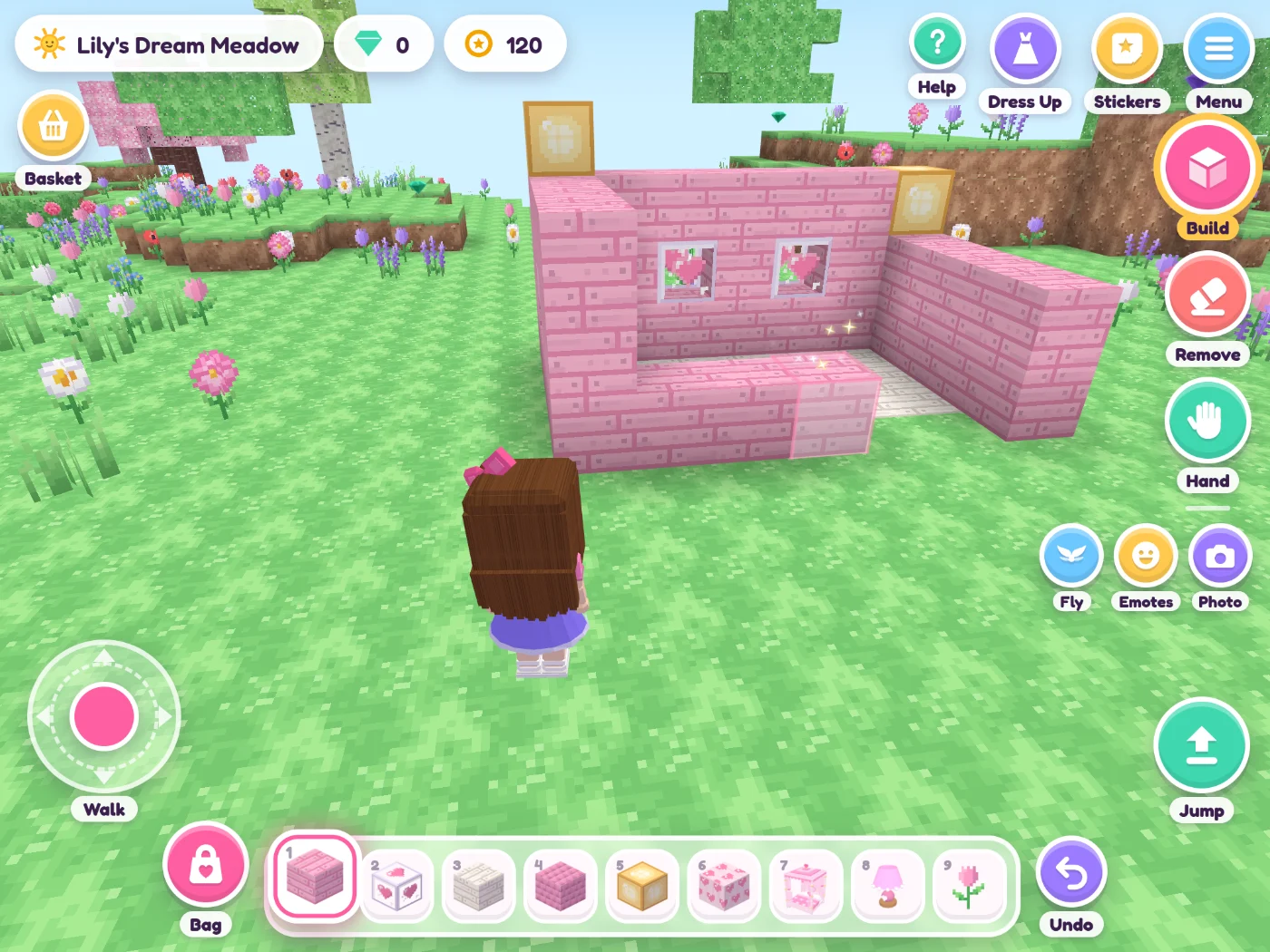 Playing on an iPad: a girl with long brown hair stands next to a pink house she is building, with heart windows and a white floor. A new row of pink planks is growing along the front. On screen: the walk joystick, the Bag, a row of blocks to pick from, Undo, and the Build, Remove and Hand buttons.